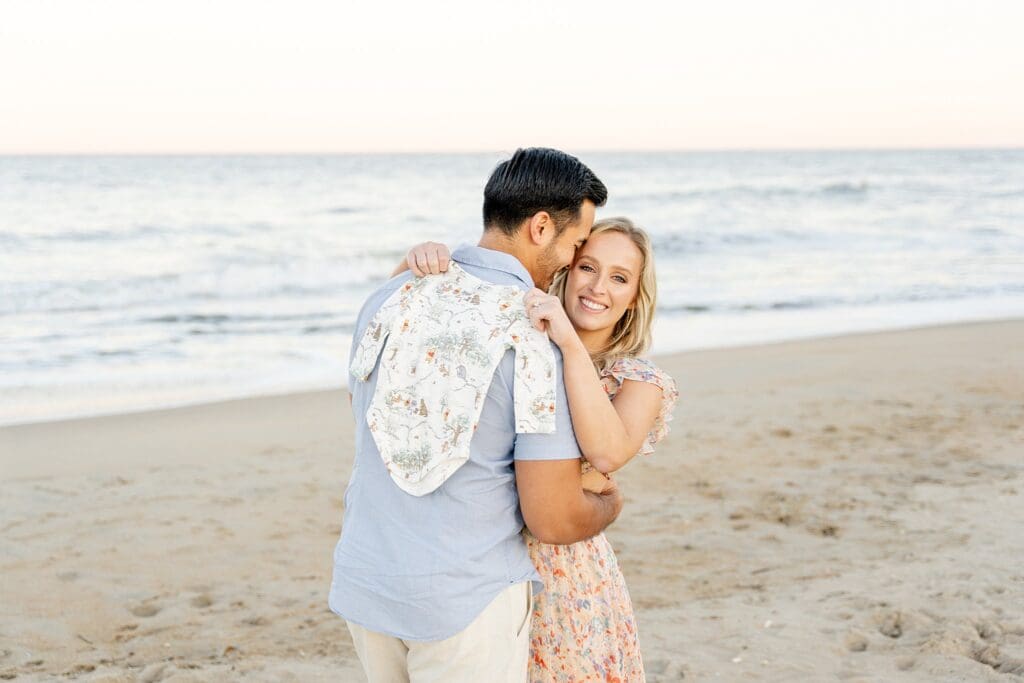 Couple holding baby outfit at golden hour session at Virginia beach