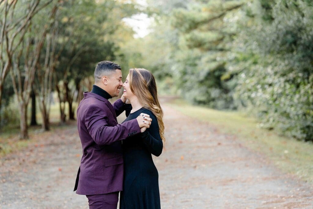 Couple walking along tree-lined path in formal black dress and purple suit