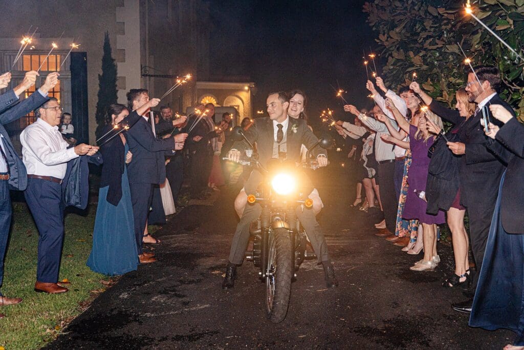 Sparkler send-off with bride and groom riding away on motorcycle