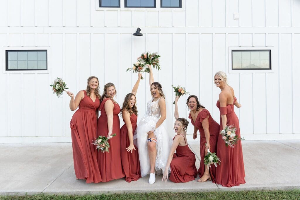 Bride and bridesmaids together in front of white barn at golden hour