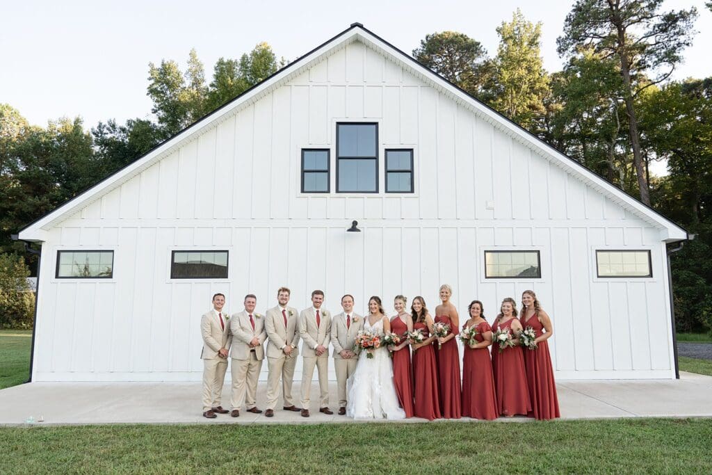 Full wedding party together in front of white Barns of Kanak at golden hour