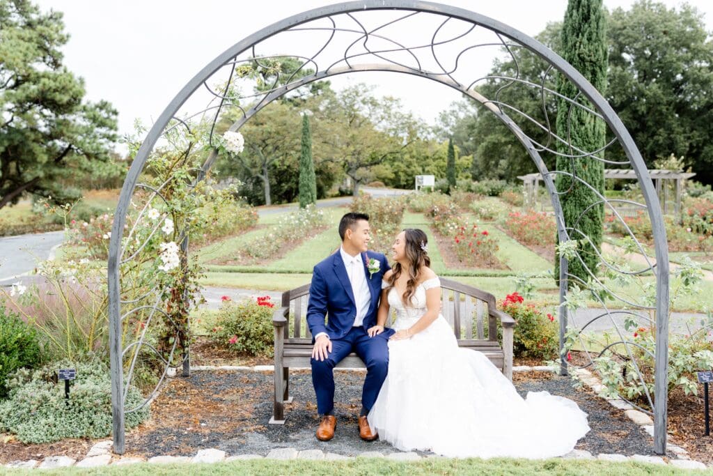 Bride and groom smiling at each other on bench at Norfolk Botanic Garden